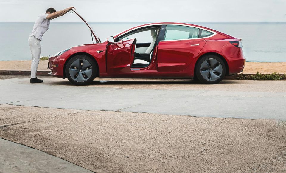 Person opening the bonnet of a broken down red electric car by the beach