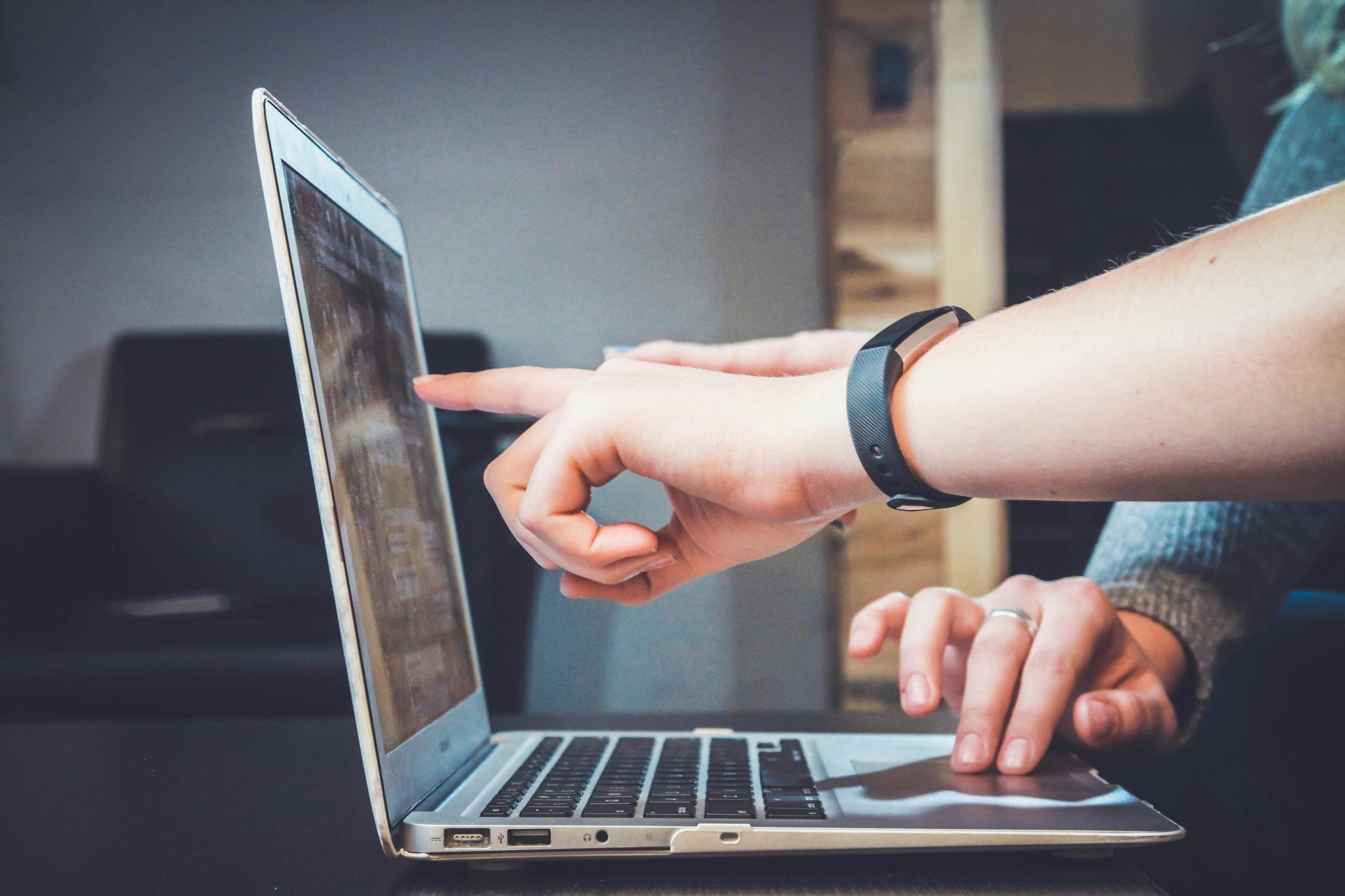 Close-up of two people collaborating on a laptop, with one person pointing at the screen to discuss information or review details.